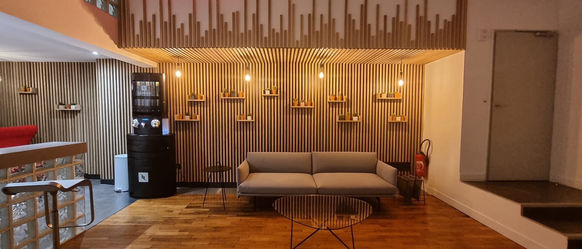Le coin salon de l'atrium, un canapé gris devant un mur à lattes de bois, sous une enseigne lumineuse On Air