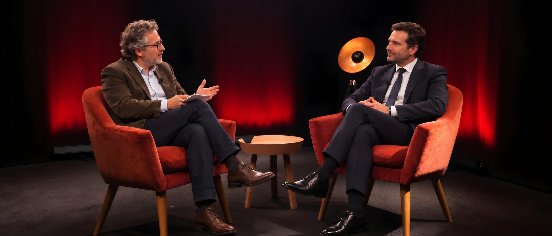 Un journaliste interroge un dirigeant, face à face dans deux fauteuils rouges sur le plateau