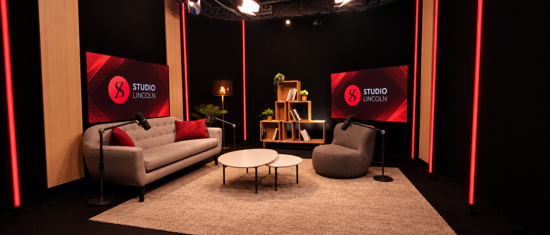 Un salon de podcast avec canapé, fauteuil, micros sur pied et deux écrans aux couleurs du studio
