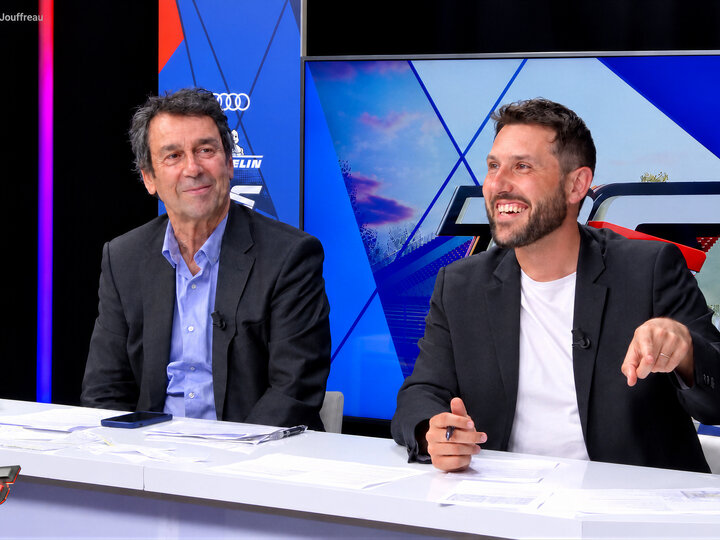Deux chroniqueurs à la table du plateau, devant le décor d'une émission de sport automobile