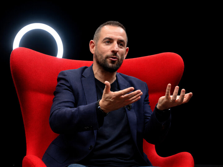 Un homme en interview, assis dans un fauteuil rouge devant un anneau lumineux